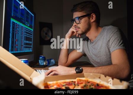 Pensive young developer in glasses using computer and coding at home Stock Photo