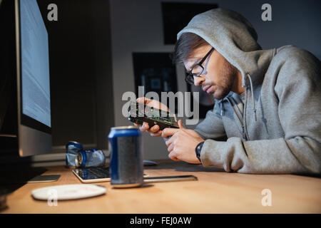 Serous pensive young man in glasses thinking and looking on broken hard disk at home Stock Photo