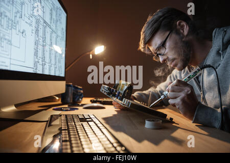 Focused young man in glasses repairing motheboard with soldering iron Stock Photo