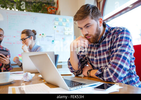 Concentrated bearded young man using laptop while his friends studying together Stock Photo