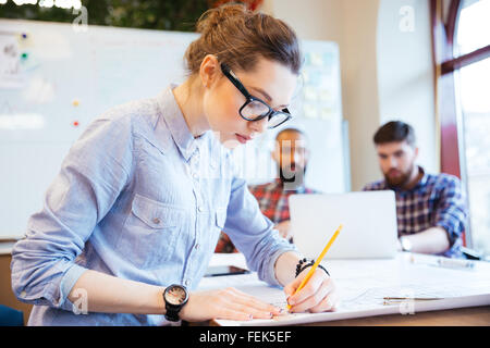 Woman engineer working on blueprint in office with colleagues on background Stock Photo