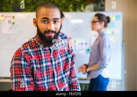Young afro american man standing in office with colleagues on background Stock Photo