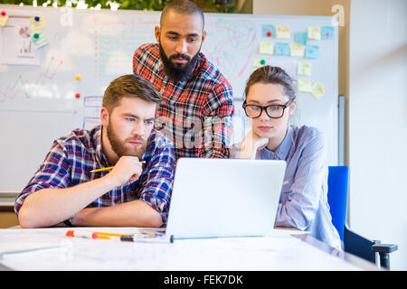 Focused serious multiethnic group of young people sitting and working with one laptop together Stock Photo
