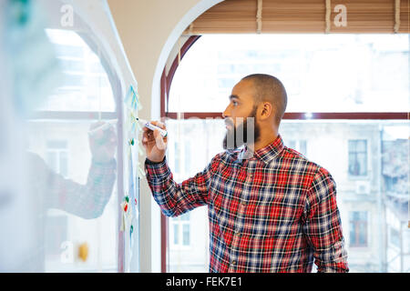 Profile of handsome african man with beard standing and writing on whiteboard Stock Photo