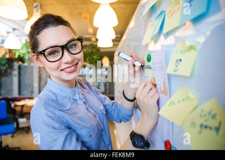 Happy businesswoman making notes on whiteboard in office and looking at camera Stock Photo