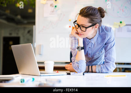 Cute lovely young female student in glasses studying with laptop in classrom Stock Photo