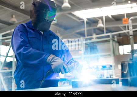 Welder in protective workwear using welding torch in steel factory Stock Photo