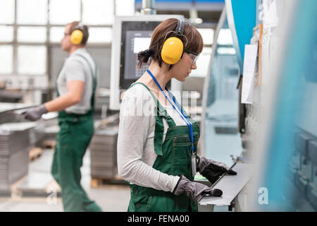 Female worker with ear protectors holding metal part in factory Stock Photo