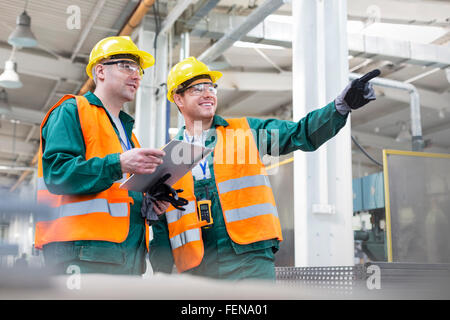 Workers in protective workwear talking with clipboard in factory Stock Photo
