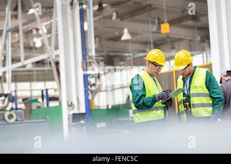 Workers in protective workwear talking with clipboard working in factory Stock Photo
