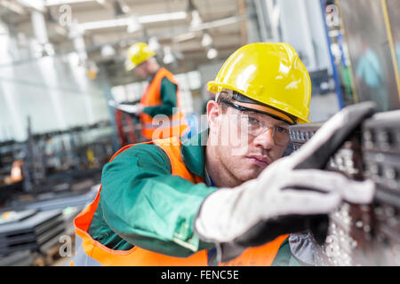 Focused worker examining steel part in factory Stock Photo