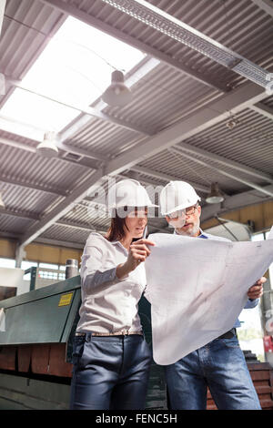 Engineers reviewing blueprints in factory Stock Photo