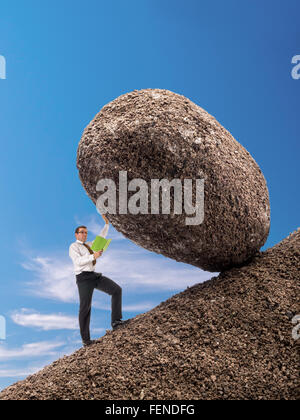 Businessman reading a book standing on slope blocking easily giant boulder with one hand from falling down Stock Photo