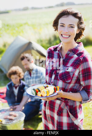 Portrait smiling woman with vegetable skewers at campsite Stock Photo