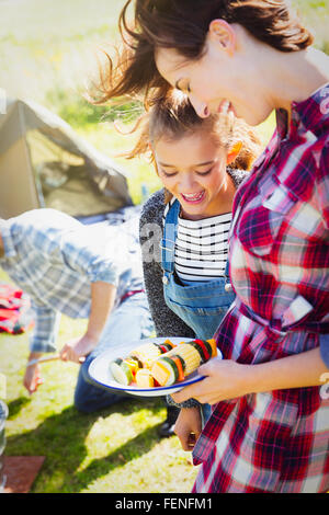 Mother and daughter with vegetable skewers at campsite Stock Photo