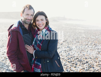Portrait smiling couple hugging on sunny rocky beach Stock Photo