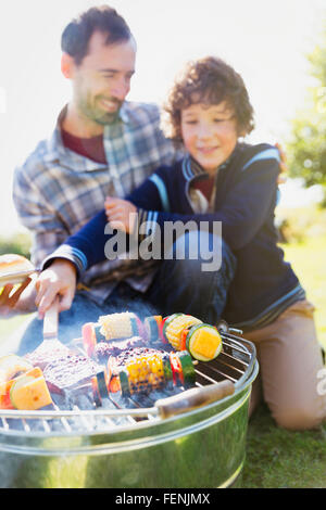 Father and son barbecuing hamburgers and vegetable skewers Stock Photo