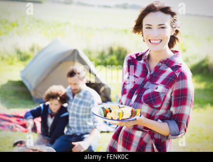 Portrait smiling woman with vegetable skewers at sunny campsite Stock Photo