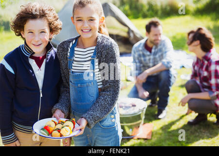 Portrait smiling brother and sister with vegetable skewers at campsite Stock Photo