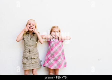 Portrait of two cute sisters pulling faces in front of white wall Stock Photo