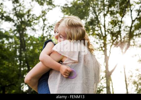 Mid adult woman carrying sleeping daughter in park Stock Photo