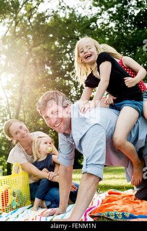 Father giving daughters piggyback at family picnic in park Stock Photo
