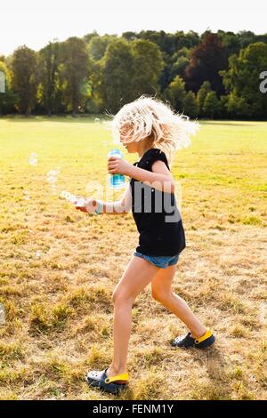 Girl waving bubble wand and making bubbles in park Stock Photo