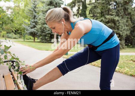 Mature woman training and touching toes on park bench Stock Photo