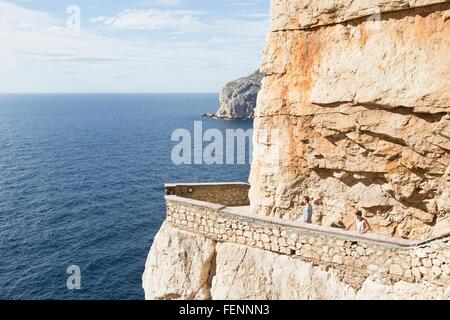 Young men by ocean on balcony carved into cliff, Grotta di nettuno (Neptune's Grotto), Capo Caccia,Sardinia,Italy Stock Photo