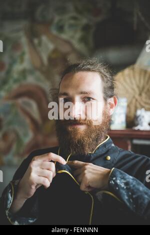 Portrait of bearded mid adult man buttoning up clay covered jacket, looking at camera smiling Stock Photo