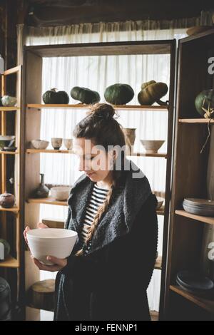 Young woman holding ceramic dish in front of shelves displaying clay pots and pumpkins
