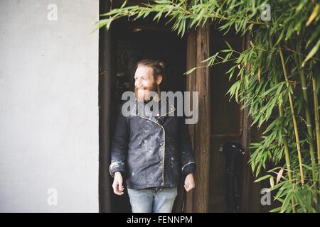 Bearded man standing in doorway looking away smiling Stock Photo