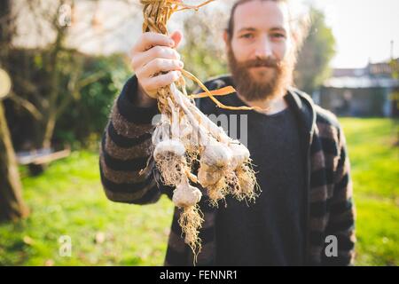 Bearded mid adult man in garden holding freshly picked garlic bulbs looking at camera smiling Stock Photo