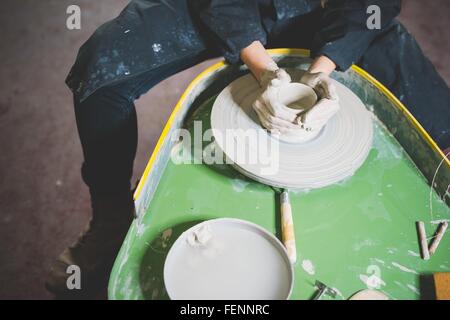 High angle view of young woman, waist down, sitting at pottery wheel making clay pot Stock Photo