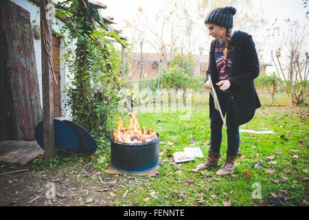 Side view of young woman wearing knit hat by fire in metal barrel Stock Photo