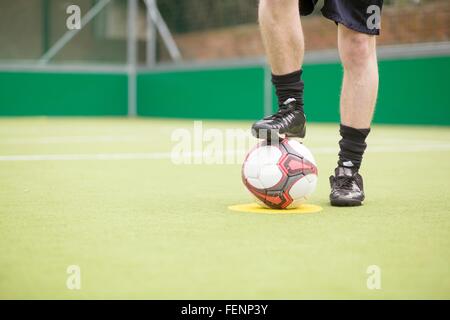 Young man on urban football pitch, foot on football, low section Stock Photo