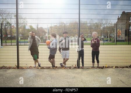 Group of young adults taking break from sport, leaning against fence