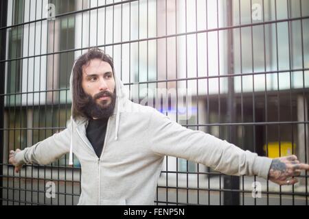 Mid adult man standing against fence, looking away Stock Photo