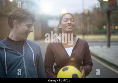 Young man and woman walking in street, holding football Stock Photo
