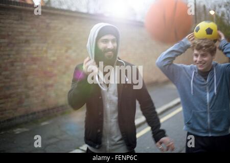 Two men walking in street, holding football Stock Photo