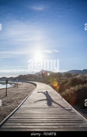 Woman jumping mid air over beach boardwalk, Villasimius, Sardinia, Italy Stock Photo