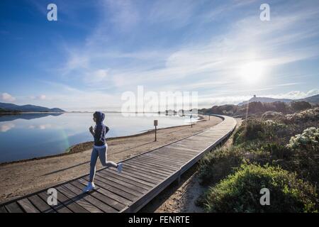 Young female runner running on beach boardwalk, Villasimius, Sardinia, Italy Stock Photo