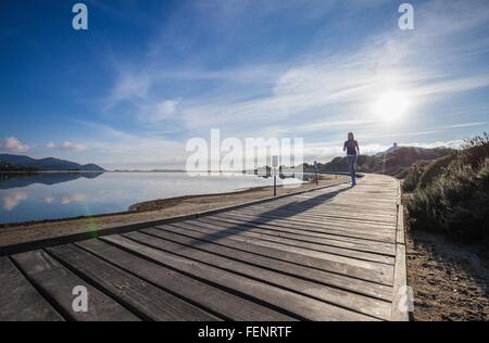Female runner running along beach boardwalk, Villasimius, Sardinia, Italy Stock Photo