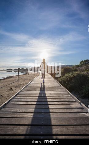 Female runner and her shadow running along beach boardwalk, Villasimius, Sardinia, Italy Stock Photo