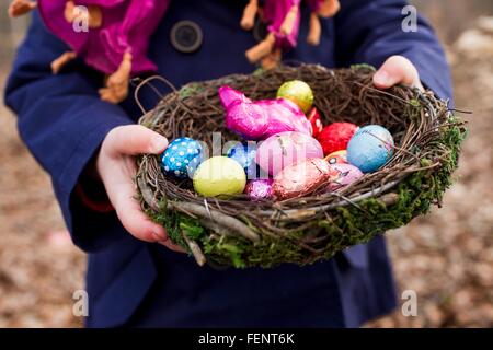 Cropped shot of female toddler holding basket nest of easter eggs in forest Stock Photo