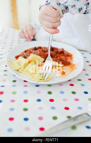 Cropped shot of female toddler eating ravioli at table Stock Photo