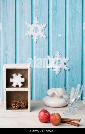 Red apples, cinnamon sticks, wine glasses, pine cone, paper snowflakes on blue wall Stock Photo