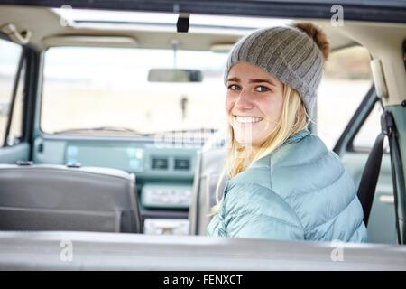 Portrait of young woman in car at beach wearing knit hat