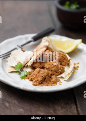Plate of Goan pork dish with naan bread, lemon slice, coriander and chilli Stock Photo
