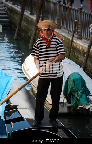 A gondoliere holding his remo (oar) wearing his blue & white striped shirt and boater with a blue band in Venice, Italy Stock Photo